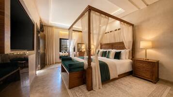 A four-poster bed with a canopy, a television mounted on the wall, and a wooden nightstand with a lamp.