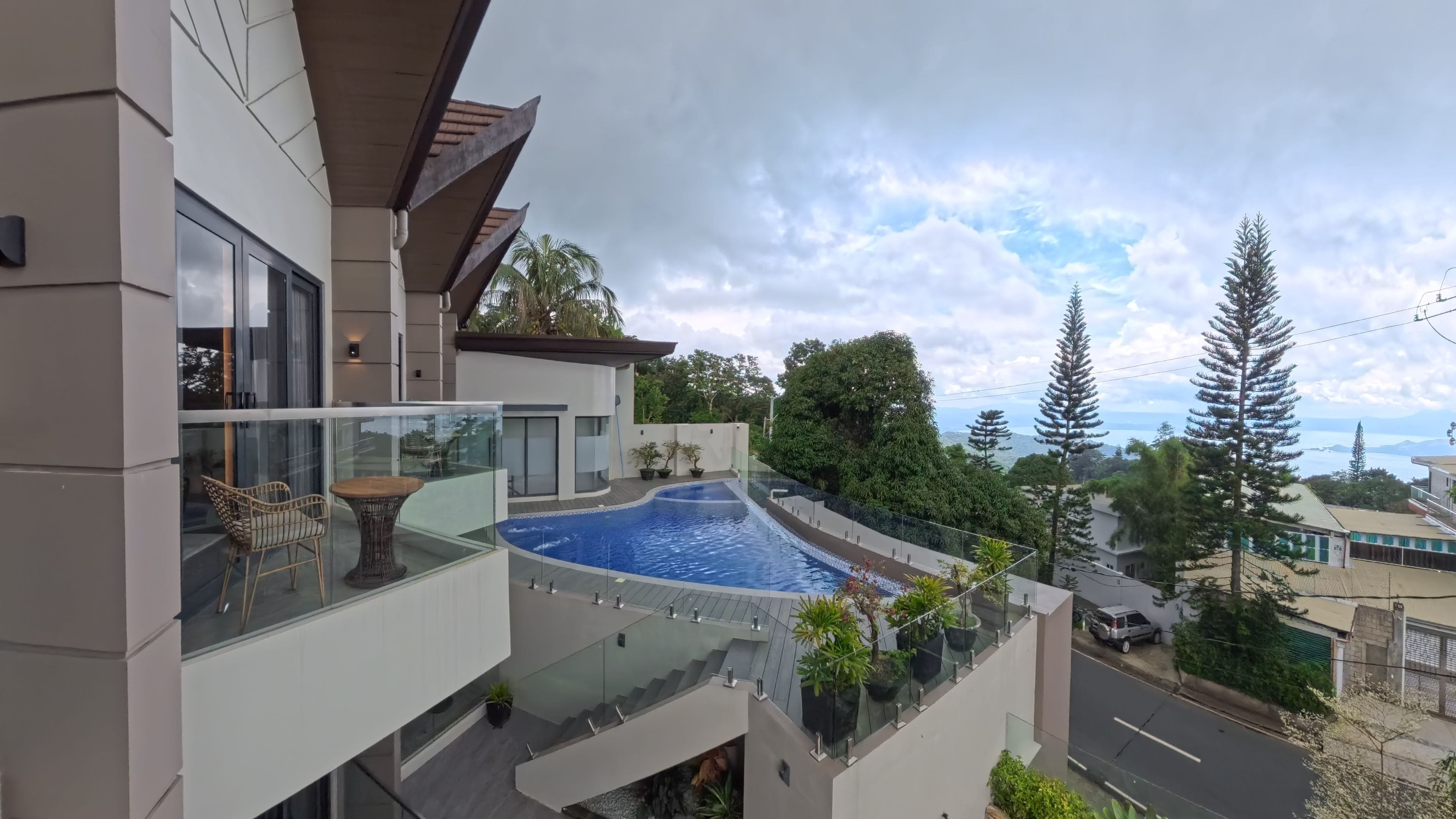 Un moderno edificio residencial con balcón de vidrio, piscina y vista del paisaje circundante.