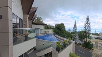 Un moderno edificio residencial con balcón de vidrio, piscina y vista del paisaje circundante.
