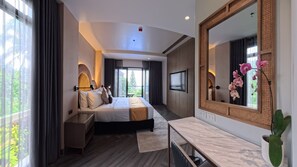Habitación de hotel moderna con una cama grande, televisión, baño y balcón con vista a zonas verdes.