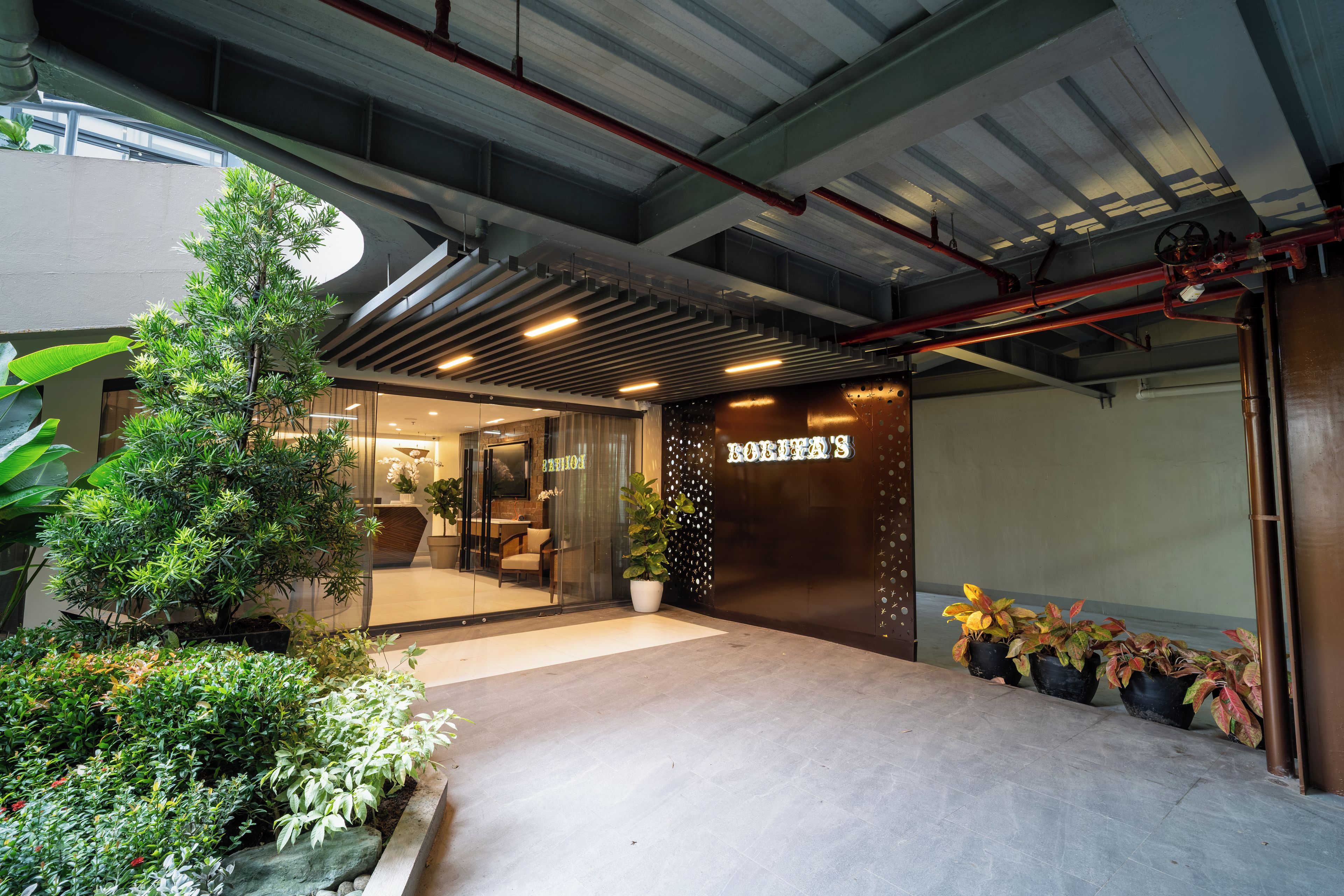Una entrada moderna de edificio con puerta de vidrio, plantas en macetas y un letrero que dice 'HOTEL'.