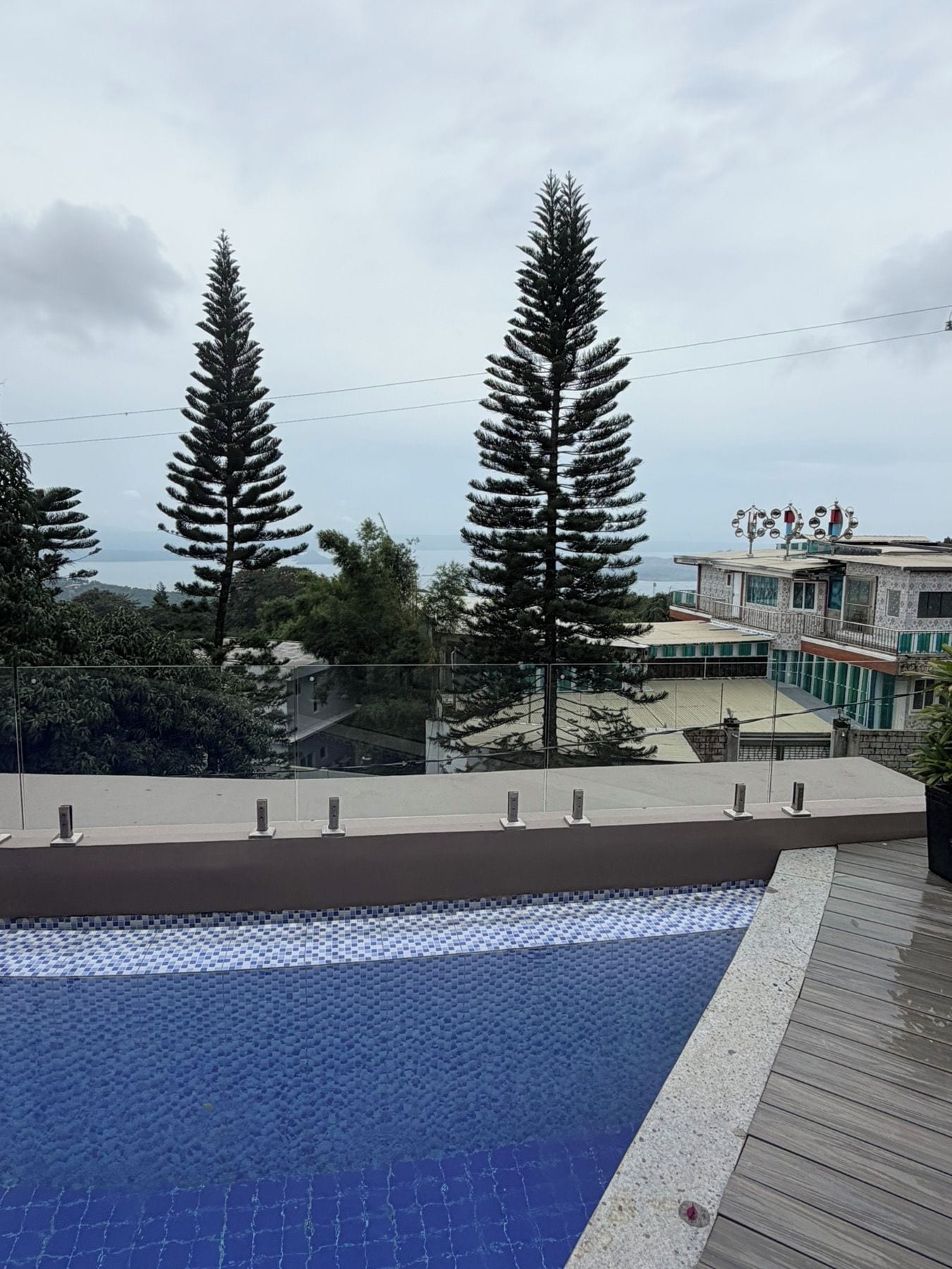 Ein Schwimmbecken mit gefliestem Sonnendeck, umgeben von Bäumen und einem Gebäude mit Balkon.