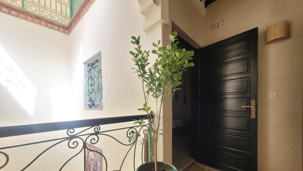 Un pasillo con barandilla decorativa, una planta en maceta, una puerta negra y baldosas con diseño.