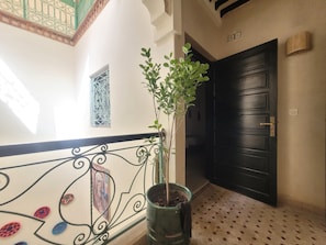 A hallway with a decorative railing, a potted plant, a black door, and patterned floor tiles. - Riad Dar Benbrahim (Marrakech)