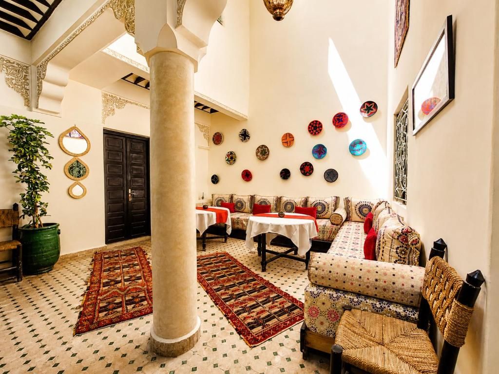 A traditional interior with a high ceiling, a large column, a sofa set, a dining table, and a wall decorated with circular plates.
