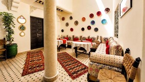 Un interior tradicional con techo alto, una columna grande, un conjunto de sofás, una mesa de comedor y una pared decorada con platos redondos.