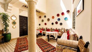 A traditional interior with a high ceiling, a large column, a sofa set, a dining table, and a wall decorated with circular plates.