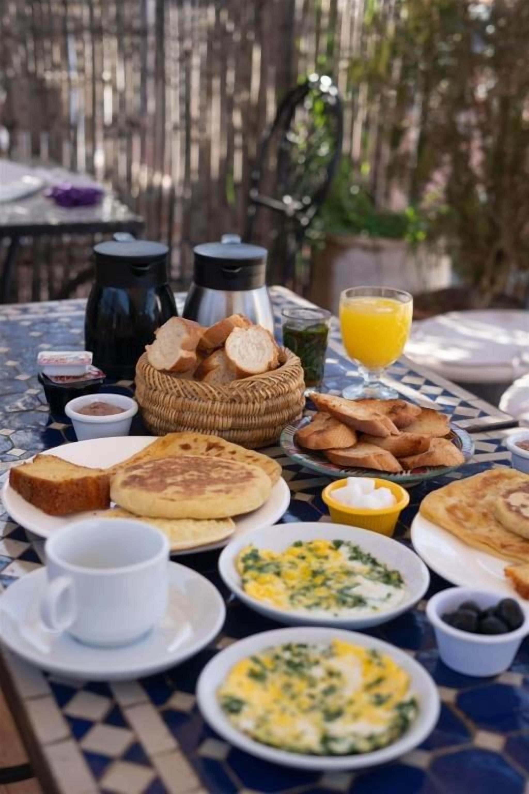 A table set with breakfast items including toast, eggs, and juice, with a wicker basket and coffee pots in the background.