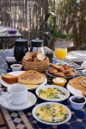 A table set with breakfast items including toast, eggs, and juice, with a wicker basket and coffee pots in the background. - Riad Dar Benbrahim (Marrakech)