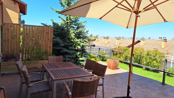 Un patio exterior con una mesa y sillas de madera, un paraguas grande y vistas a edificios cercanos.