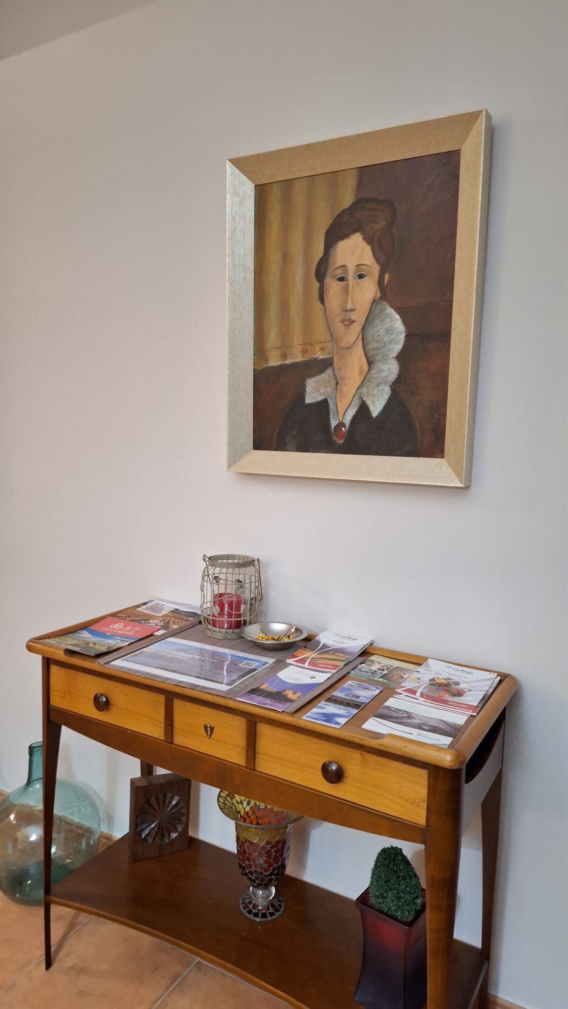 A wooden console table with a framed painting above it, a small vase, and a potted plant.