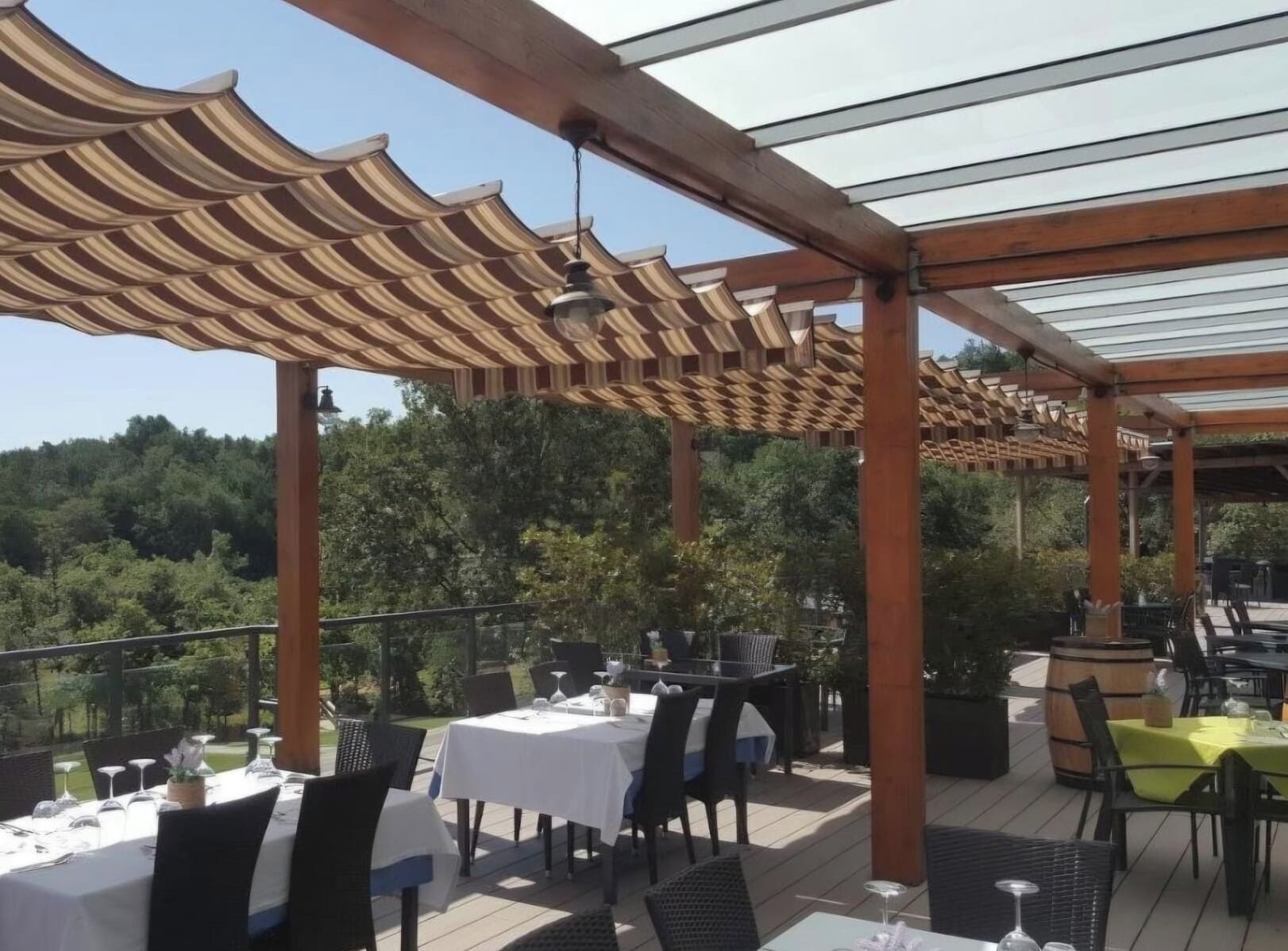 An outdoor dining area with tables and chairs, a pergola structure, and a view of the surrounding landscape.