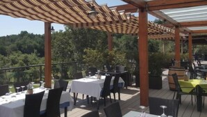 Een buiten eetgedeelte met tafels, stoelen, een pergola en uitzicht op het omliggende landschap.