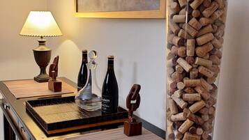 A room with a desk, a lamp, a bottle of wine, a glass bottle, and a vase filled with corks.