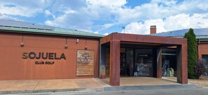 Un edificio con un letrero que dice 'SOJUELA CLUB GOLF' y el logotipo de 'BANTOS RESTAURANT'.