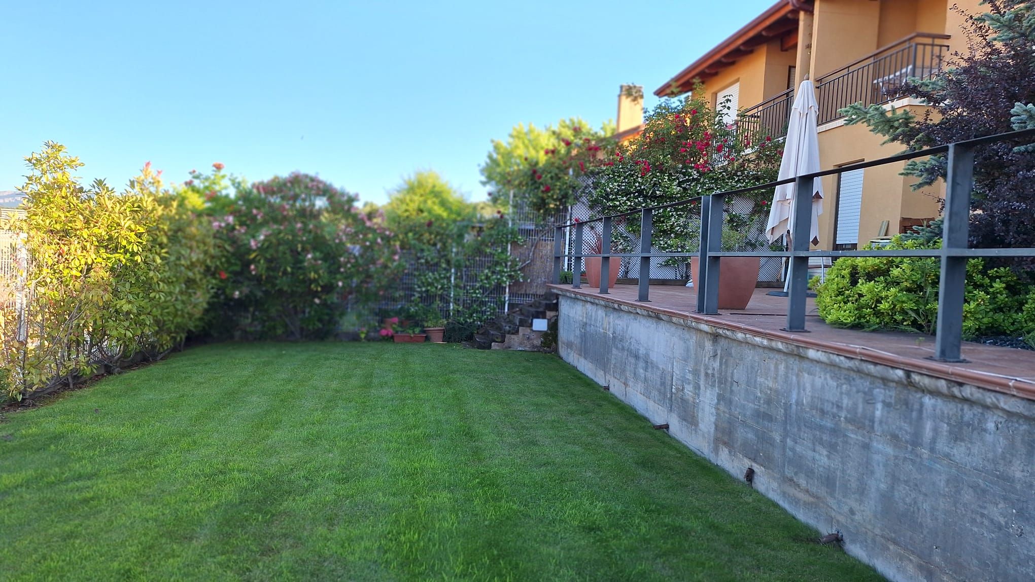 Ein gepflegter Rasen Garten mit einer Betonmauer, einem Metallzaun und einem Balkon mit Gartenmöbeln.