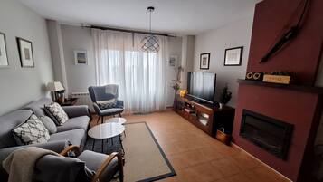 A living room with a sofa, armchairs, a coffee table, a TV, and a fireplace.