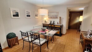 Een eetruimte met een glazen tafel, zwarte stoelen, een houten kast en ingelijste foto’s aan de wanden.