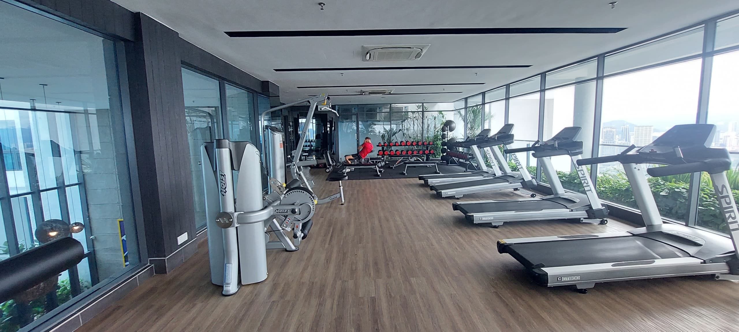 Un gimnasio con máquinas de cardio, equipo de pesas y una persona haciendo ejercicio.