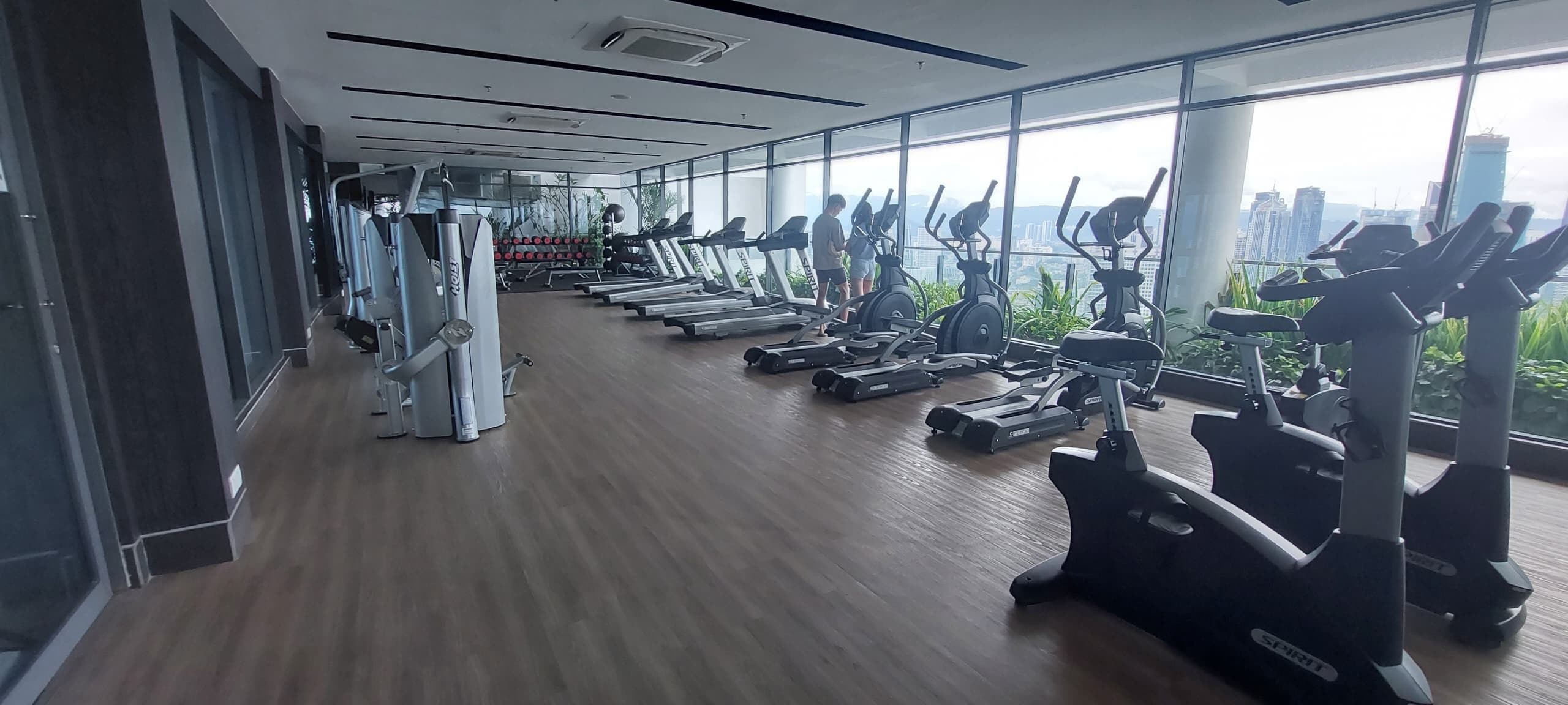 Un gimnasio con máquinas de cardio, pesas y un amplio ventanal con vista a la ciudad.