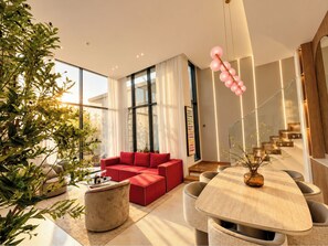 A modern living room with a red sofa, a glass coffee table, and a dining area with a wooden table and chairs. - Pool Days. City Nights. Your Private VILLA Escape (دبي)