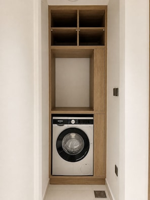 Ein kleiner Hauswirtschaftsraum mit einer integrierten Waschmaschine und Holzregalen darüber.