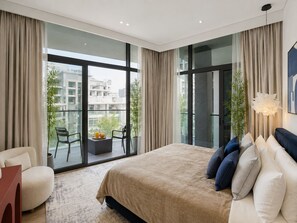 A modern bedroom with a large bed, a seating area with a chair and a small table, and a balcony with a view of the city. - Pool Days. City Nights. Your Private VILLA Escape (دبي)
