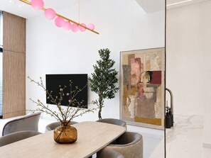 A modern dining area with a wooden table, chairs, a vase with branches, a potted plant, and a large abstract painting on the wall. - Pool Days. City Nights. Your Private VILLA Escape (دبي)