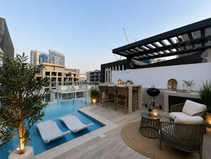 A rooftop pool area with lounge chairs, a bar, and a grill. - Pool Days. City Nights. Your Private VILLA Escape (دبي)