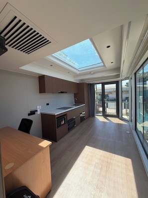 A modern kitchen with a skylight, wooden cabinets, a built-in oven, and a dining area with a table and chairs.