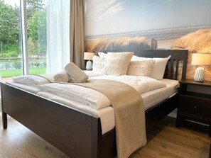 Ein Schlafzimmer mit einem großen Bett, einem Nachttisch, einer Lampe und Blick ins Freie.