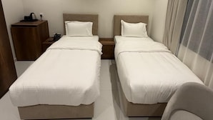 Ein Hotelzimmer mit zwei Betten, einem Nachttisch, einem Sessel und einem Fenster mit Vorhängen.