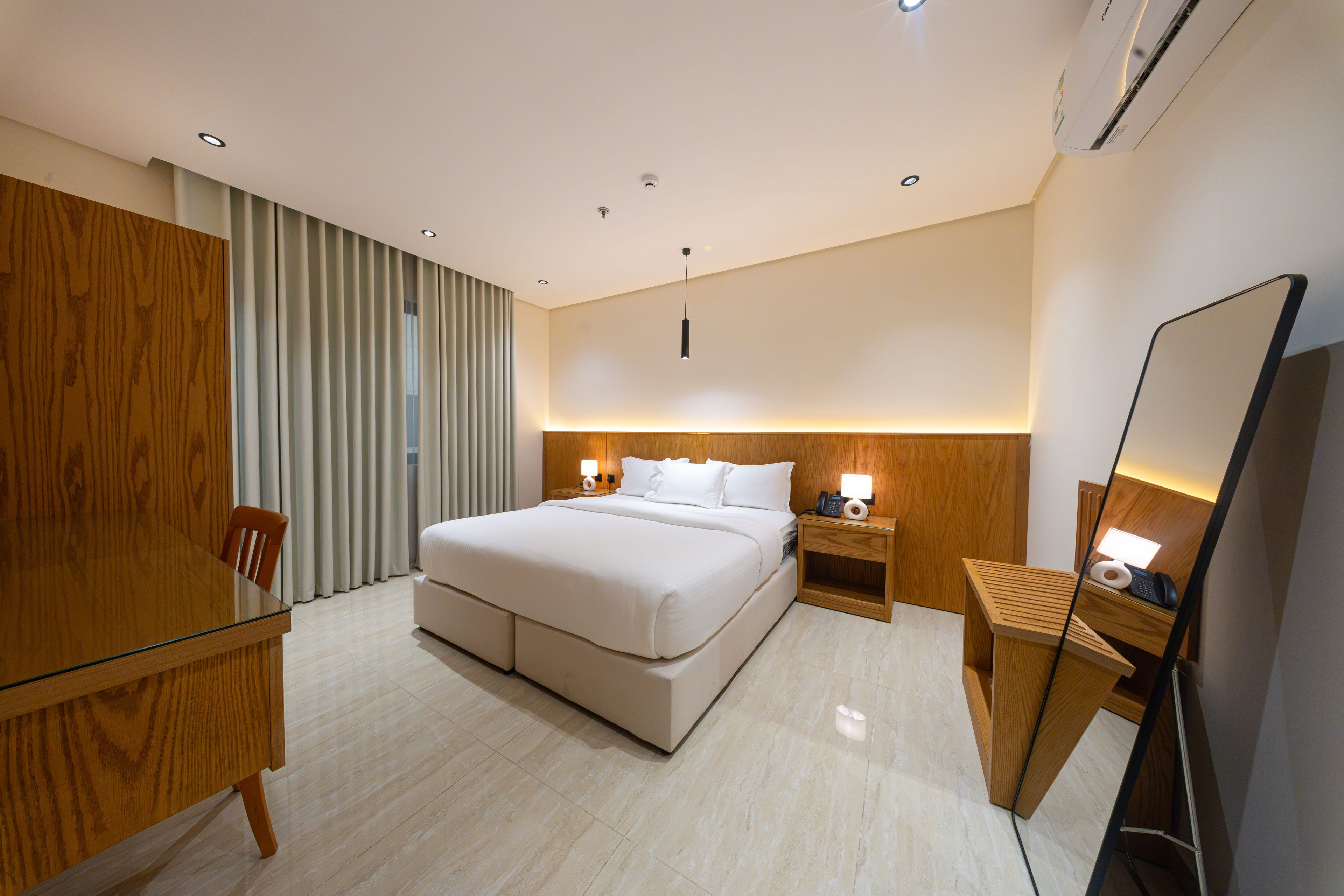 A hotel room with a large bed, bedside tables, a desk, and a mirror.