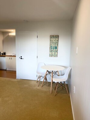 Una habitación con una puerta blanca, una pequeña mesa redonda con dos sillas blancas y un cartel en la pared con varias palabras.