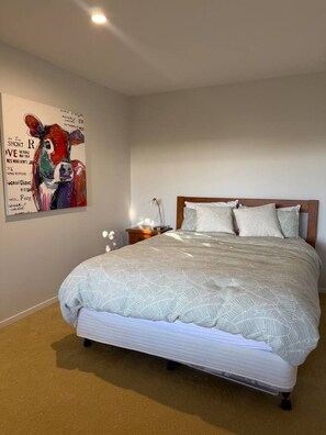 Un dormitorio con una cama, una mesita de noche, una lámpara y una obra de arte en la pared.
