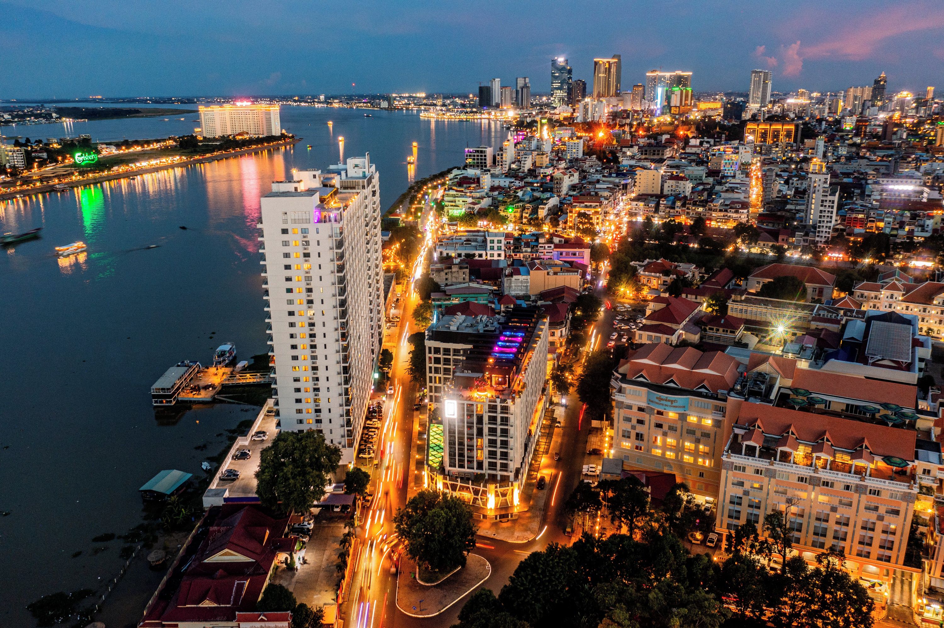 A cityscape with a prominent high-rise hotel, a river, and a busy waterfront area.