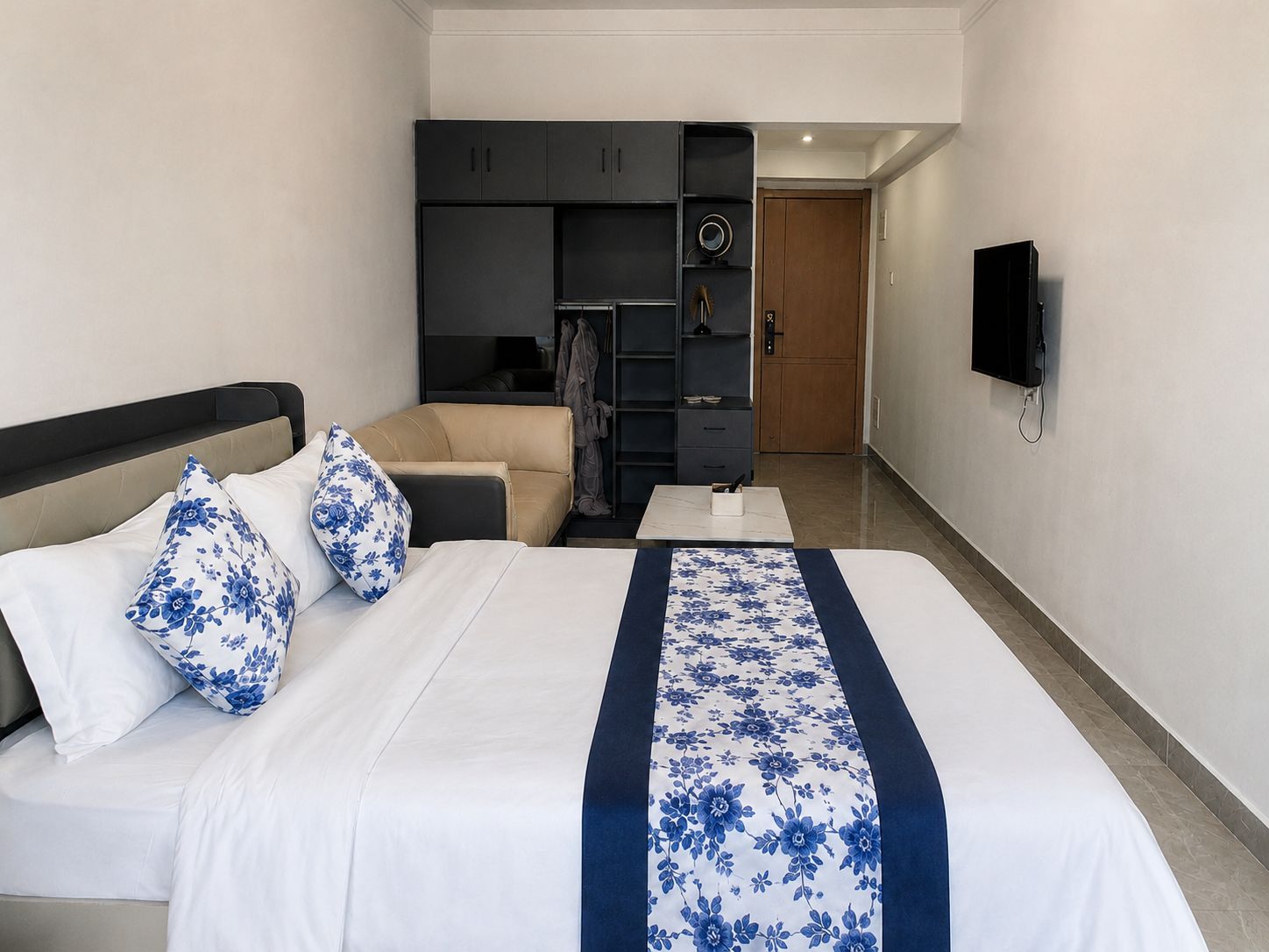 A hotel room with a bed, a sofa, a desk, and a TV mounted on the wall.