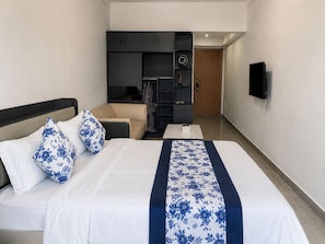 Una habitación de hotel con cama, sofá, escritorio y televisión instalada en la pared.