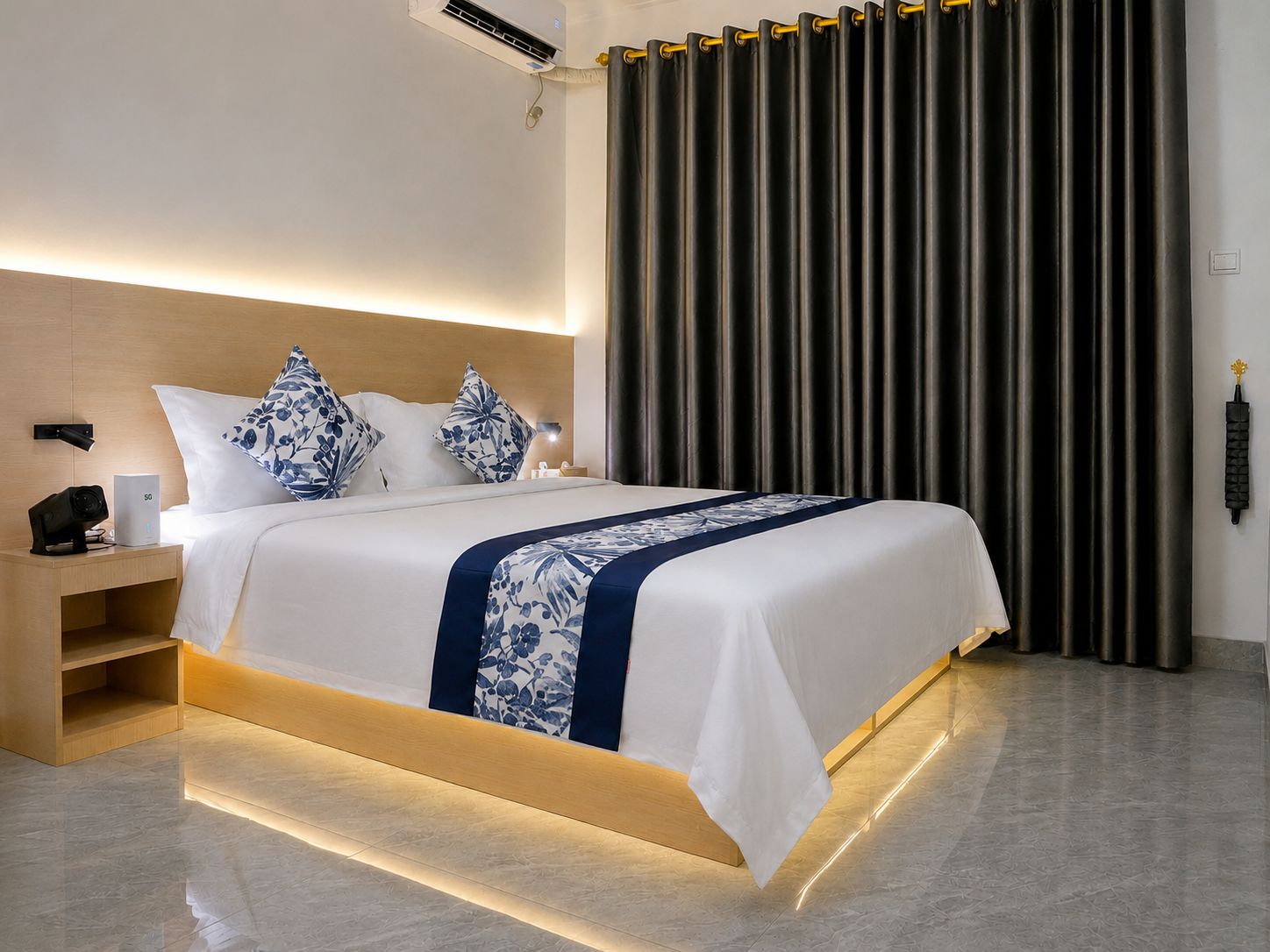 A modern hotel room with a bed, bedside table, and a large window with curtains.