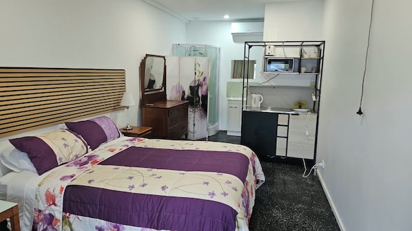 Quarto de hotel com cama, penteadeira, espelho e uma pequena cozinha.