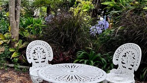 A white metal outdoor seating area with a table and two chairs, surrounded by lush greenery and trees. - Self-contained room in beautiful rural Queensland location with beautiful views (Illinbah)