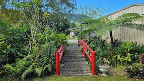 Uma ponte de madeira com grades vermelhas que leva a um edifício rodeado por vegetação exuberante.
