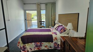 Quarto de hotel com cama, mesa de cabeceira, luminária e vista para o exterior.