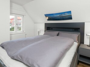 A bedroom with a bed, bedside tables, a wall-mounted artwork, and a window. - 272 - Apartment Lighthouse (Juist)