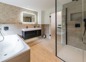 Ein modernes Badezimmer mit einem großen weißen Waschbecken, einer schwarzen Waschtischunterschrank und einer Duschkabine aus Glas. Die Wand hat eine Steinoptik.