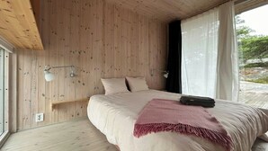 Une chambre avec un plafond en bois, un lit recouvert d’un plaid rose et deux lampes de chevet.