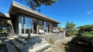 Une maison moderne dotée d’une terrasse en bois, de grandes fenêtres et d’un espace extérieur aménagé et abrité.