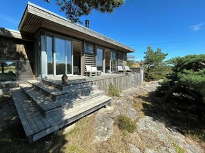 A modern house with a wooden deck, large windows, and a covered outdoor seating area. - Architect-designed cabin at Holmetangen (Vesterøy)