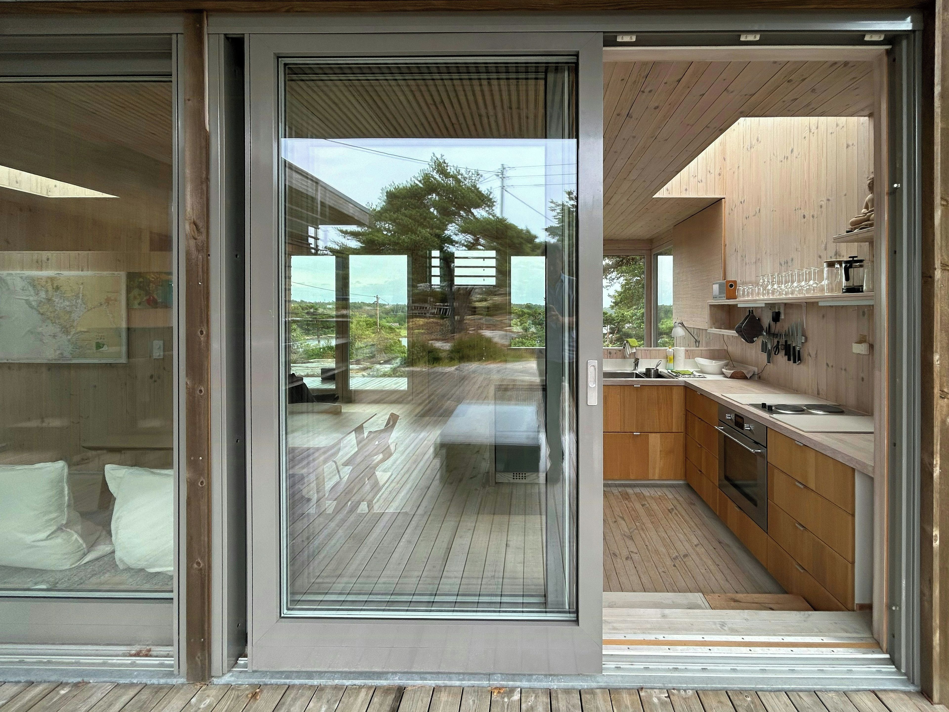 Une cuisine moderne avec des meubles en bois, un four encastré et une grande fenêtre donnant sur une terrasse.