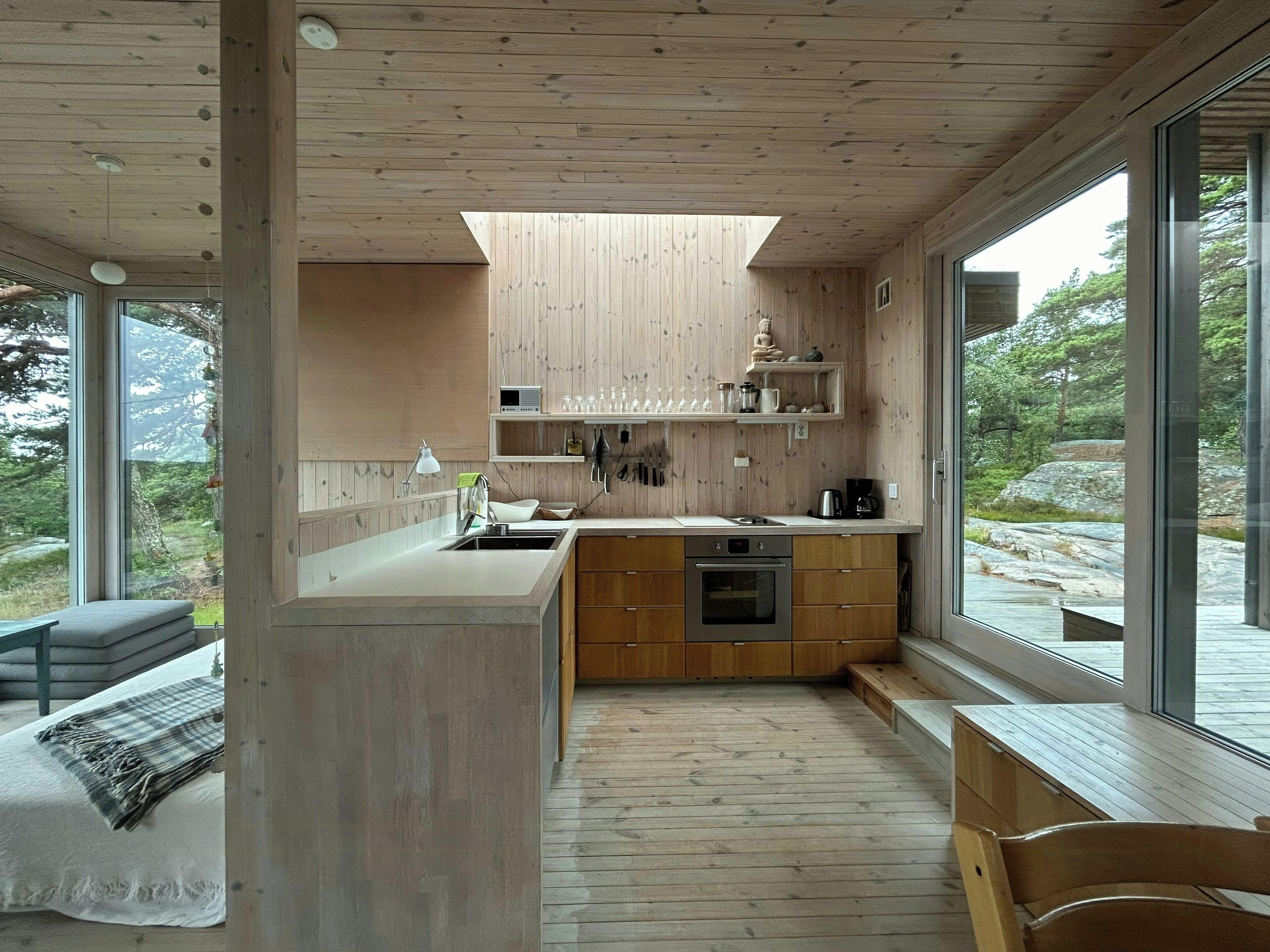 Eine moderne Küche mit Holzausstattung, einem Einbauofen und einem großen Fenster mit Blick auf eine natürliche Landschaft.